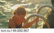 Woman in swimsuit climbing metal ladder from sea at sunset near rocky shore in summer Croatia. Стоковое видео, видеограф Igor Tichonow / Фотобанк Лори