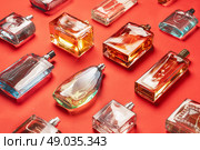 An elegant display features a diverse collection of glass perfume and cologne bottles, each uniquely shaped and filled with various fragrances. The bottles are arranged on a vivid red background, Стоковое фото, фотограф Владимир Разгуляев / Фотобанк Лори