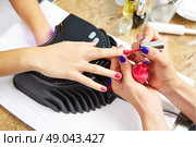 Nails painting with UV dry lamp in blue light woman hands at nail salon. Стоковое фото, агентство Ingram Publishing / Фотобанк Лори