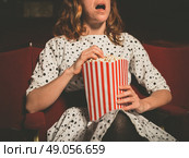A young woman is sitting on the front row in a movie theater and is watching an exciting film while eating popcorn. Стоковое фото, агентство Ingram Publishing / Фотобанк Лори
