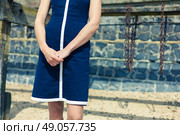 A young woman wearing a blue dress is standing on the beach on a sunny day by an old wooden structure with rusty chains hanging from it. Стоковое фото, агентство Ingram Publishing / Фотобанк Лори