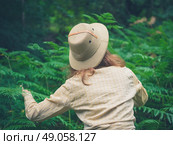 A young woman wearing a safari hat is exploring a forest with lots of green ferns. Стоковое фото, агентство Ingram Publishing / Фотобанк Лори