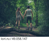 A young couple is holding hands and are  standing on a log in the forest. Стоковое фото, агентство Ingram Publishing / Фотобанк Лори