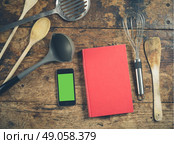A selection of kitchen utensils on a wooden table with a book and a smart phone with a green screen chromakey. Стоковое фото, агентство Ingram Publishing / Фотобанк Лори
