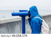 A person wearing a blue jacket and hood is using a telescope on the coast. Стоковое фото, агентство Ingram Publishing / Фотобанк Лори