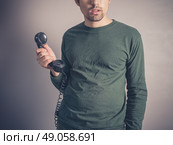 A concerned and worried looking young man is holding the receiver of a vintage rotary phone. Стоковое фото, агентство Ingram Publishing / Фотобанк Лори