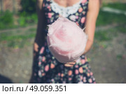 A young woman wearing a dress is standing outside with a candyfloss on a sunny summer day. Стоковое фото, агентство Ingram Publishing / Фотобанк Лори