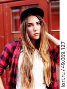 Lifestyle portrait of fashionable blonde girl with ombre hair wearing a rock red shirt, black cap, white t-shirt and denim shorts having fun outdoors in the city. Swag style. Стоковое фото, агентство Ingram Publishing / Фотобанк Лори