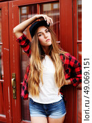 Lifestyle portrait of fashionable blonde girl with ombre hair wearing a rock red shirt, black cap, white t-shirt and denim shorts having fun outdoors in the city. Swag style. Стоковое фото, агентство Ingram Publishing / Фотобанк Лори