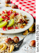 Bowl of oatmeal with slices of kiwi and pomegranate and scattered the table with hazel and cashew nuts. Dish of oat flakes. Стоковое фото, агентство Ingram Publishing / Фотобанк Лори