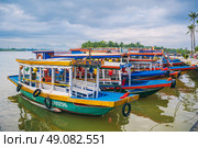 Traditional wooden Vietnamese boats on the Thu Bon River in the old town in Hoi An in Vietnam. Vietnam, Hoi An - December 1, 2024. Редакционное фото, фотограф Корчагина Анастасия / Фотобанк Лори
