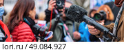 A close-up image of a journalist holding a microphone while interviewing someone at an outdoor event, surrounded by other journalists and members of the public. Стоковое AI-изображение, AI-художник Данила Большаков / Фотобанк Лори