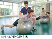 Two men assisting friends exercising on aerobic balls. Стоковое фото, агентство Ingram Publishing / Фотобанк Лори