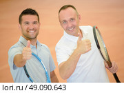 Two men holding tennis rackets making thumbs up gesture. Стоковое фото, агентство Ingram Publishing / Фотобанк Лори
