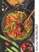 Sliced  green French beans dish with tomatoes sauce and wooden cooking spoon. Stewed French beans "spaghetti"  in vintage cooking pot on dark rustic background, top view.  Vegetarian food concept. Стоковое фото, агентство Ingram Publishing / Фотобанк Лори