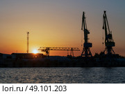 Port cranes for cargo transshipment on the mooring line of the Astrakhan port on the right bank of the Volga River against the background of the setting sun on a summer evening, Astrakhan, Russia. Стоковое фото, фотограф Ula Ulachka / Фотобанк Лори