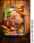 Roast lamb leg with vegetables and fresh herbs in blue casserole bowl on rustic wooden background, top view. Стоковое фото, агентство Ingram Publishing / Фотобанк Лори