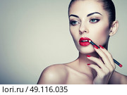 Beautiful woman paints lips with lipstick. Beautiful woman face. Makeup detail. Beauty girl with perfect skin. Red lips and nails manicure. Стоковое фото, агентство Ingram Publishing / Фотобанк Лори