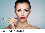 Beautiful woman paints lips with lipstick. Beautiful woman face. Makeup detail. Beauty girl with perfect skin. Red lips and nails manicure. Стоковое фото, агентство Ingram Publishing / Фотобанк Лори