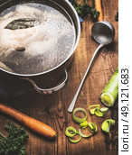Broth with whole boiled chicken in cooking pot with ingredients and ladle on kitchen table, top view. Стоковое фото, агентство Ingram Publishing / Фотобанк Лори