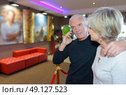 Couple in cinema lobby, man on cellphone. Стоковое фото, агентство Ingram Publishing / Фотобанк Лори