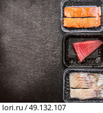 Various of raw fish fillets : salmon, tuna and codfish in plastic boxes on dark rustic background, top view, border, place for text. Healthy Seafood concept. Стоковое фото, агентство Ingram Publishing / Фотобанк Лори