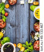 Salad making, food frame with oil,vinegar, tomatoes, basil and cheese on blue rustic wooden background, top view, vertical. Стоковое фото, агентство Ingram Publishing / Фотобанк Лори