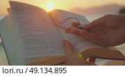Hands hold an open Bible and a cross pendant at the beach during a sunset as the light shines over the pages. Стоковое видео, видеограф Igor Tichonow / Фотобанк Лори