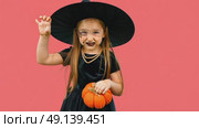 A child wearing a witch's hat holds knitting pumpkin, gleefully celebrating Halloween. Стоковое AI-видео, аниматор Ирина Старикова / Фотобанк Лори