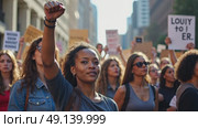 A woman in a protest march raises her right arm in a fist pump, her face filled with determination. The background is a blurred crowd of people walking on street. Стоковое AI-видео, аниматор Sergey Grishin / Фотобанк Лори
