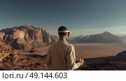 Man wearing VR headset in desert landscape, merging technology with nature, exploration and innovation theme with vast rocky terrain under clear sky. Стоковое AI-изображение, AI-художник Катерина Бондарец / Фотобанк Лори