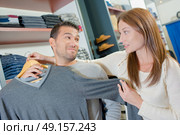 Couple in clothes shop, lady holding jumper against man. Стоковое фото, агентство Ingram Publishing / Фотобанк Лори
