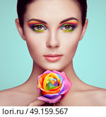 Portrait of beautiful young woman with rainbow rose. Bright colors. Long eyelashes, vivid colorful eyeshadows. Rainbow make up. Multicolored flowers. Стоковое фото, агентство Ingram Publishing / Фотобанк Лори