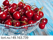 Red sweet cherry in crystal vase on a blue wooden background. Стоковое фото, агентство Ingram Publishing / Фотобанк Лори