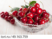Red sweet cherry and green leaves in crystal vase on a wooden background. Стоковое фото, агентство Ingram Publishing / Фотобанк Лори