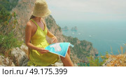 Woman reads map and points toward Faraglioni cliffs and sea in summer Capri, Italy. Стоковое видео, видеограф Igor Tichonow / Фотобанк Лори
