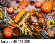 Thanksgiving dinner table with Roasted whole turkey ,sauce with grilled autumn vegetables,corn ,cutlery , decoration pumpkin, autumn leaves and flowers arrangements on rustic background, top view. Стоковое фото, агентство Ingram Publishing / Фотобанк Лори
