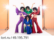 A group of girls in colorful flared suits and afro wigs pose in a photo studio. Disco style from the eighties or seventies. Стоковое фото, фотограф Лазаренко Светлана / Фотобанк Лори