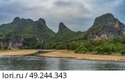 A picturesque river. Shallow pools on the sandy shore. Mountain range on the background of sky and clouds. Green forest on the slopes. China. Li River. Li Jiang. Guilin. Стоковое фото, фотограф Вера Ивановна Кубарева / Фотобанк Лори