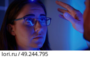A woman wearing glasses is attentively looking at a bright blue light. Стоковое AI-изображение, AI-художник Данила Большаков / Фотобанк Лори
