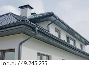 A residential house featuring a solid roof and functional gutters, designed to protect the structure from rainwater. Стоковое AI-изображение, AI-художник Данила Большаков / Фотобанк Лори