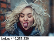 A blonde woman playfully sticks out her tongue in a snowy setting. Стоковое AI-изображение, AI-художник Данила Большаков / Фотобанк Лори