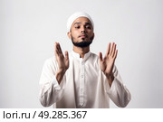 A man dressed in white cultural clothing stands with hands raised in a traditional gesture. Стоковое AI-изображение, AI-художник Данила Большаков / Фотобанк Лори