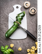 Green sliced zucchini on white cutting board with kitchen knife , top view. Healthy vegetarian cooking and eating, diet food concept. Стоковое фото, агентство Ingram Publishing / Фотобанк Лори