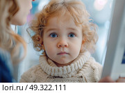 A young child with curly blond hair and striking blue eyes looks up with an expression of curiosity and innocence. Стоковое AI-изображение, AI-художник Данила Большаков / Фотобанк Лори
