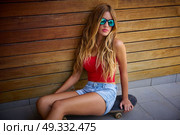 Blond teen girl sit on skateboard in a wood wall with sunglasses. Стоковое фото, агентство Ingram Publishing / Фотобанк Лори