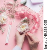 Female hands making floral arrangements with white flowers and ribbon at pastel pink background, top view. Стоковое фото, агентство Ingram Publishing / Фотобанк Лори