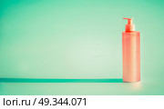 Pink cosmetic bottle with dispenser pump at mint background. Summer skin care lotion or sunblock product with copy space for design. Стоковое фото, агентство Ingram Publishing / Фотобанк Лори