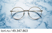 A pair of round glasses with thin gold rim, placed on a white marble surface. пара круглых очков с тонким золотым ободком, расположенных на белой мраморной поверхности. Стоковое AI-изображение, AI-художник Katsiaryna Repich / Фотобанк Лори