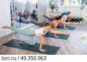 Group of young women practicing Balancing Table restorative Pose or Dandayamana Bharmanasana during yoga workout on mats. Стоковое фото, фотограф Яков Филимонов / Фотобанк Лори